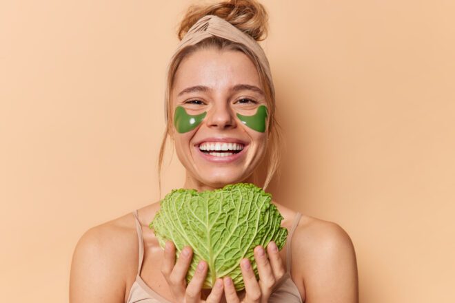 portrait cheerful young woman uses natural cosmetic beauty products holds green fresh cabbage put skin moisturising applies hydrogel patches eyes stands bare shoulders βιγκανισμός και φυτική διατροφή για υγεία και βιωσιμότητα